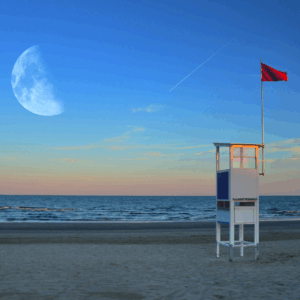 Ein verlassener Rettungsturm mit roter Warnflagge steht still am Strand, während der riesige Mond am Himmel hängt und ein Kondensstreifen leise eine Linie zieht. Das Bild wirkt wie ein eingefrorener Moment zwischen Ebbe und Flut – ein Sinnbild für das Ringen um Balance im Zeitmanagement: Die Flut der Aufgaben im Hintergrund, der Mond als stetiger Taktgeber der Zeit, die rote Flagge als Warnsignal vor Überlastung. Der Turm – Symbol für Überblick und Prioritäten – mahnt zur Ruhe und lädt ein, den eigenen Rhythmus neu zu justieren.