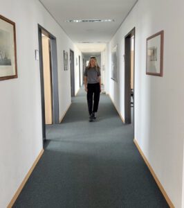 Constance Rettler betrachtet nachdenklich die Meilensteine ihres Unternehmens in einem Büroflur mit gerahmten Fotos an der Wand.
