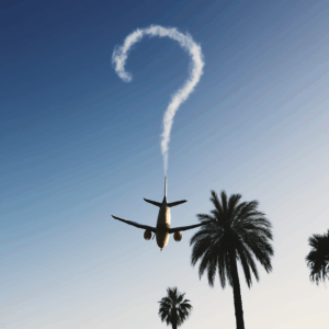 Flugzeug fliegt über Palmen in den Sonnenuntergang, hinterlässt ein Fragezeichen aus Abgasstreifen am Himmel