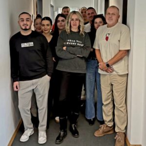 Eine Gruppe von Mitarbeitenden im DRS Büro München steht eng beisammen im Flur und blickt geschlossen in die Kamera. Die Personen wirken aufmerksam und ernst, die Atmosphäre ist konzentriert und kollegial.